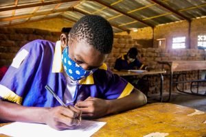 A boychild learner writes his assignment with a face mask on during class break at Mchoka primary school